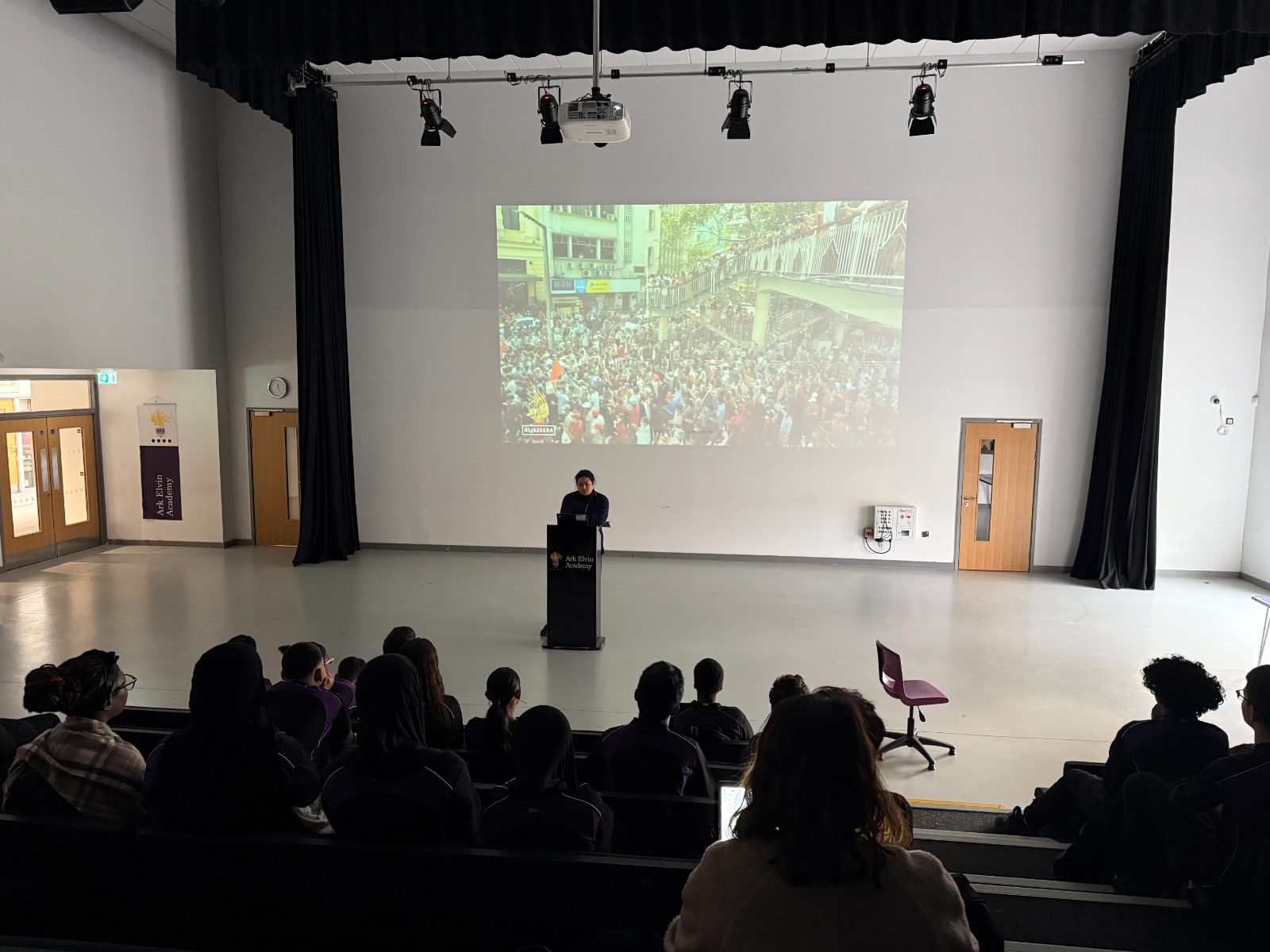 A speaker addresses students in a school assembly hall